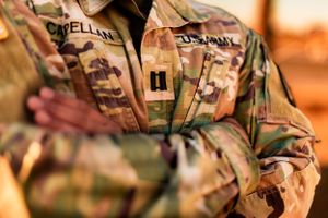 Close-up detail of name tape and rank insignia on camouflage military uniform.