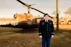 Service member in dress blues standing at attention in front of a military helicopter.