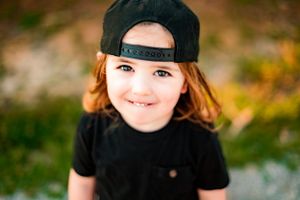 Close-up portrait of child wearing black baseball cap and t-shirt outdoors.