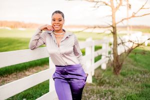 Person in athletic wear smiling while exercising outdoors near white fence.