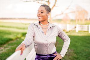 Person in business casual clothing posing outdoors by white fence during golden hour.