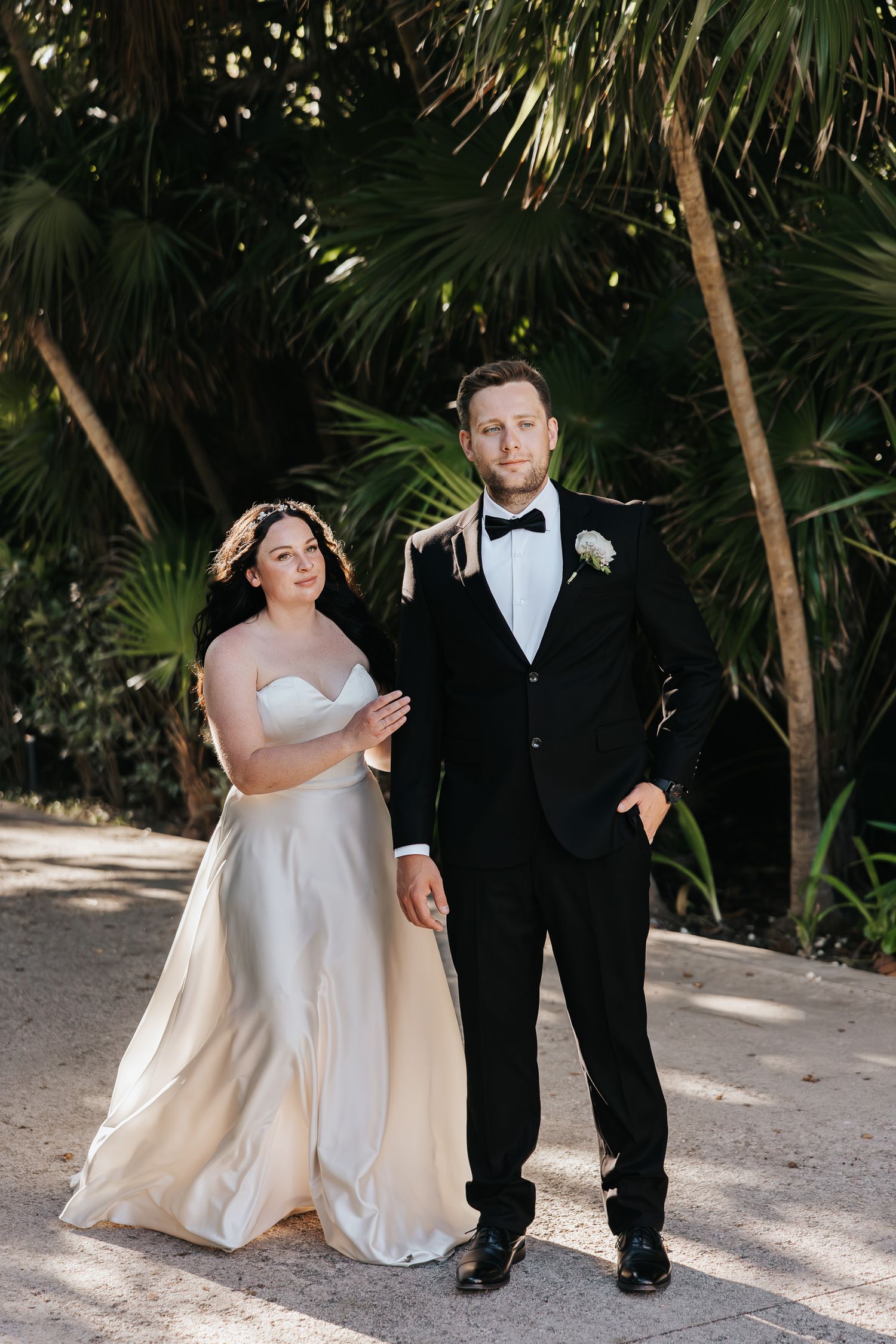Cancun Mexico Wedding
A bride in a flowing white gown and groom in black tuxedo pose together on a tropical palm-lined path.