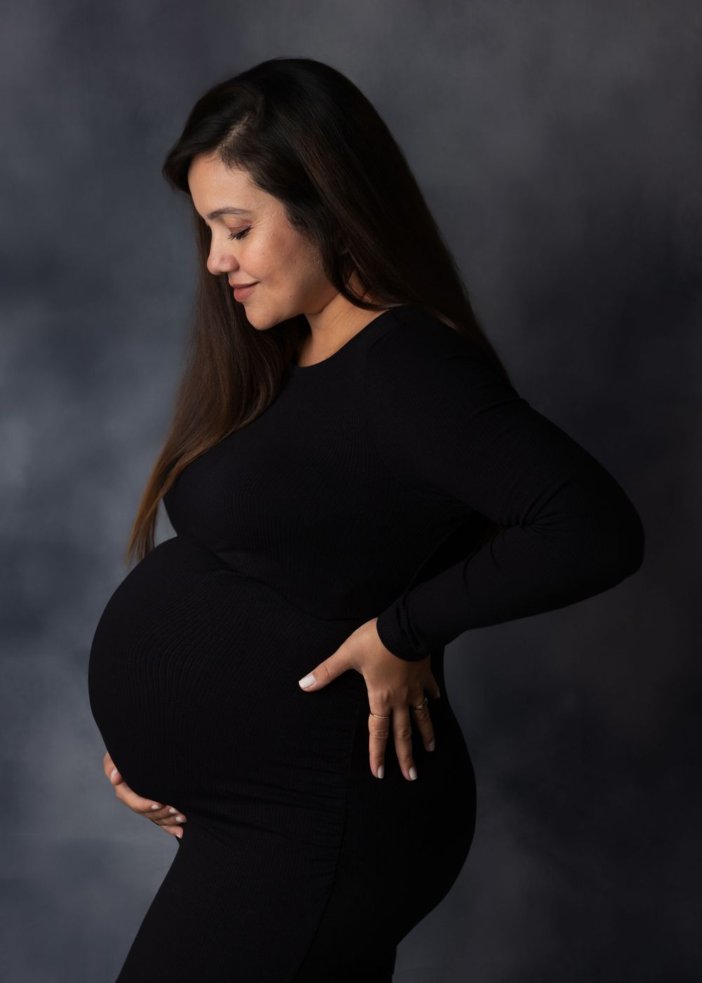 Pregnant woman in black outfit cradling her baby bump during a professional maternity photo session.