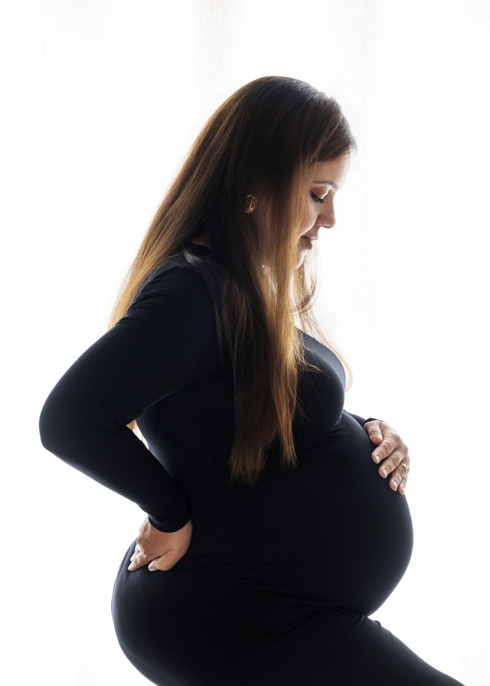 Pregnant woman in black outfit cradling her baby bump, side profile maternity photo against white background.