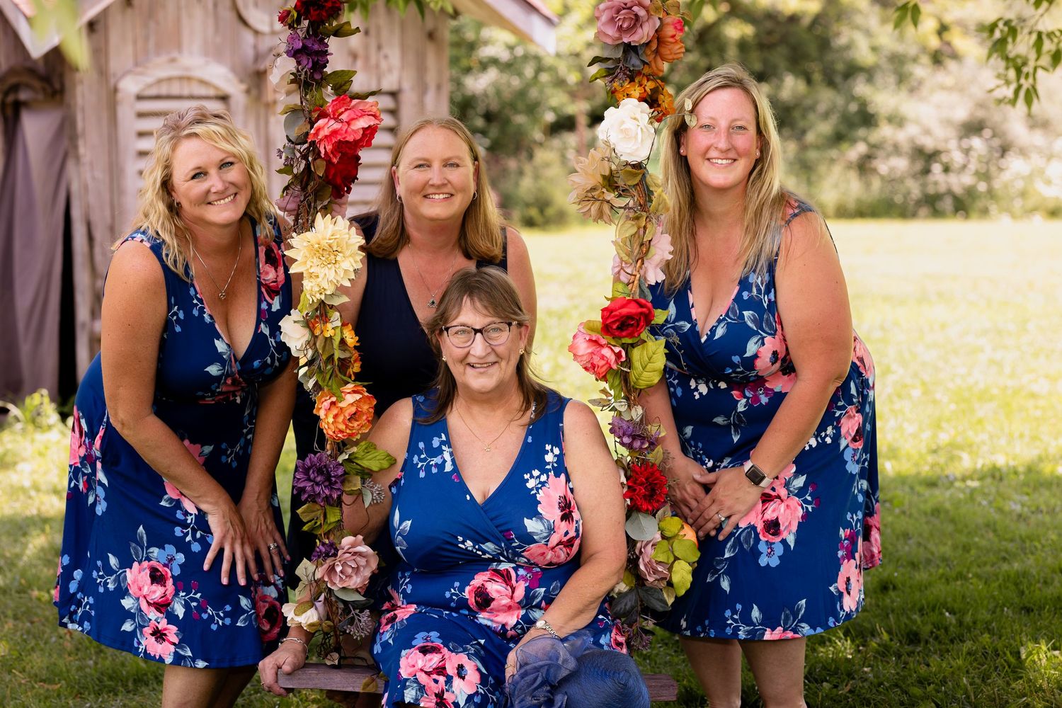 A group wearing coordinating blue floral dresses poses together by a decorated floral arch.