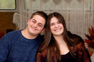 A cozy indoor portrait featuring warm smiles and casual attire against a curtained background.