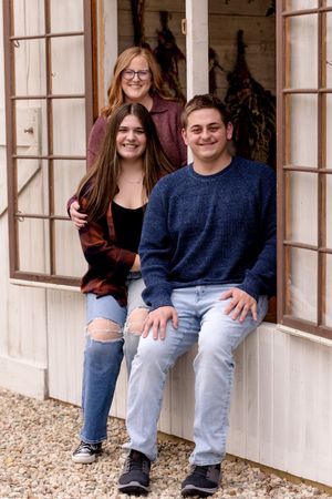 Three people pose together in a bright window frame wearing casual outfits and denim.