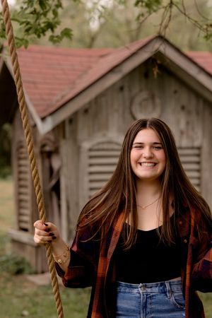 A casual outdoor portrait by a rustic wooden shed with someone holding a rope swing.