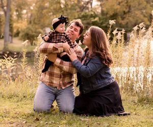 Family enjoying playful moment together in golden field during sunset photoshoot.