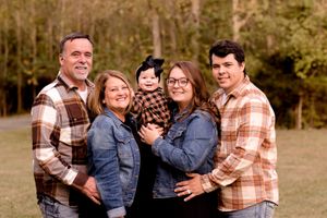 Family of five posing together in matching plaid shirts against wooded background.