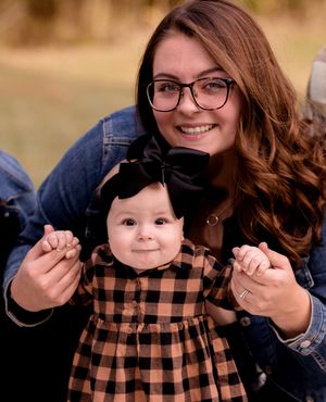 Mother and baby in matching plaid dress share sweet moment during outdoor photoshoot.