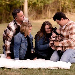 Family gathered on white blanket outdoors sharing intimate moment during photo session.
