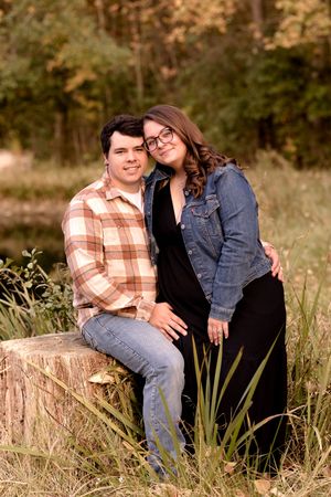 Couple sitting on tree stump in coordinated outfits during outdoor portrait session.