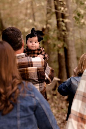 Baby in plaid dress and bow during outdoor family photoshoot.