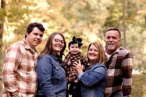 A family wearing coordinated plaid and denim outfits poses together in an autumn forest setting.