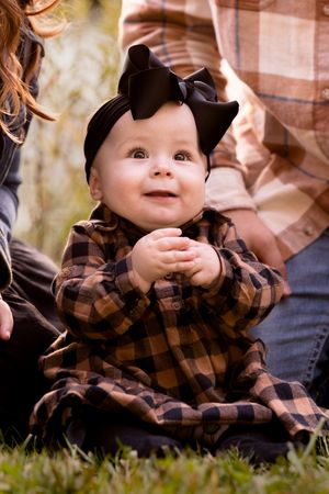 A small child in plaid and bear ears outfit smiles while being held during an outdoor photo shoot.