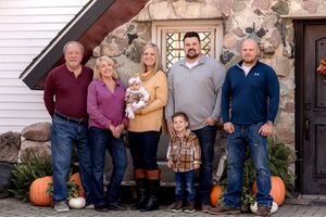Family group photo with pumpkin decorations and stone wall background.
