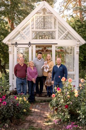 Family gathered in front of beautiful greenhouse surrounded by blooming roses.
