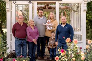 Family portrait session in a sunlit greenhouse decorated with autumn pumpkins and floral arrangements.