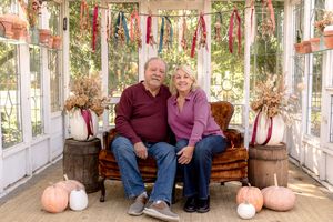 Cozy greenhouse setting with wooden benches and pink pumpkin decorations for fall family photos.