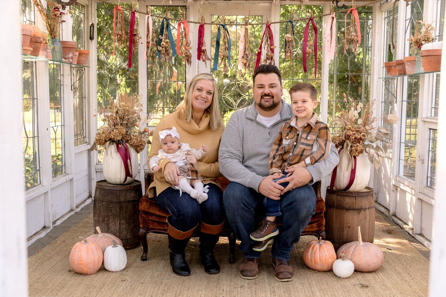 Rustic greenhouse interior decorated with hanging plants and seasonal pumpkins for family photography.