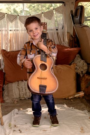 Young child posing with acoustic guitar in rustic barn setting.