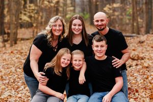 Extended family group sits casually together for portraits in an autumn forest setting.