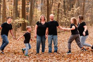 Family members strike playful poses on fallen leaves in a wooded autumn setting.