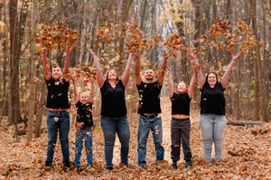 Group photo showing multiple generations standing in a line among autumn trees.