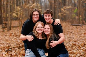 Casual family portrait with members embracing and smiling in a fall forest setting.