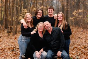 Casual family portrait with group hugging and laughing together on autumn ground.