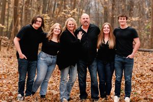 Family wearing coordinated black outfits poses together in fall forest setting.
