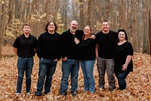 Group portrait of six people wearing matching black outfits in fall forest setting.