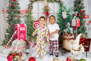 Festive Christmas scene with children in pajamas posing by decorated trees, mailbox, and holiday decor.