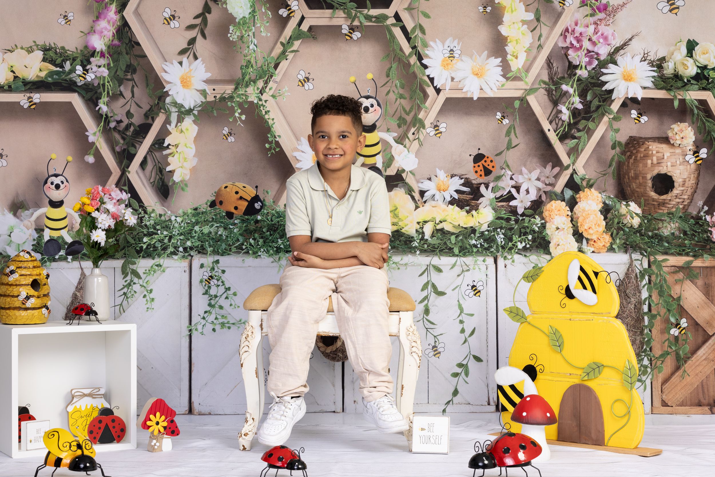 Enchanting garden-themed photo setup with hexagonal shelves, decorative bees, and ladybugs against a floral backdrop.