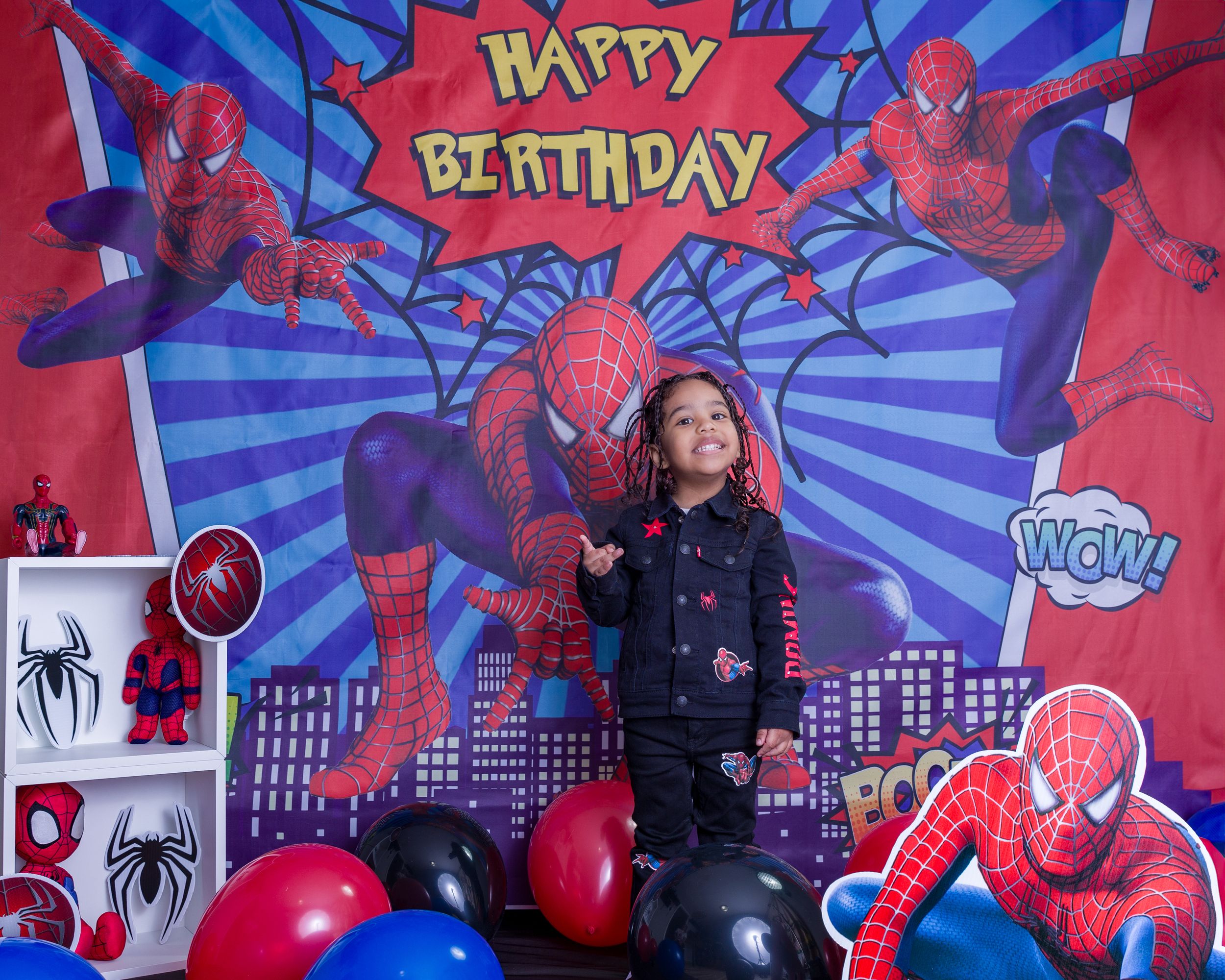 Child posing at Spider-Man themed birthday party with balloons and superhero decorations.