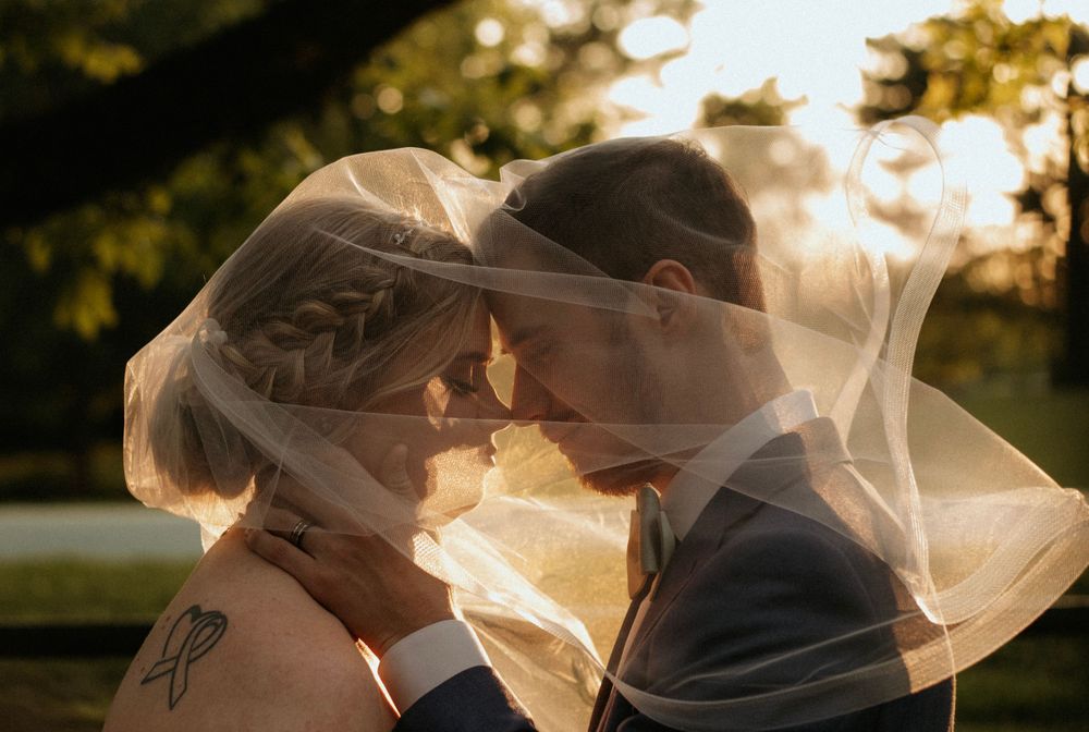 Romantic wedding couple sharing intimate moment under flowing veil at sunset.