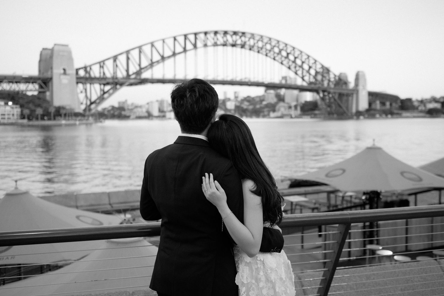 Couple embracing while admiring Sydney Harbour Bridge at sunset.