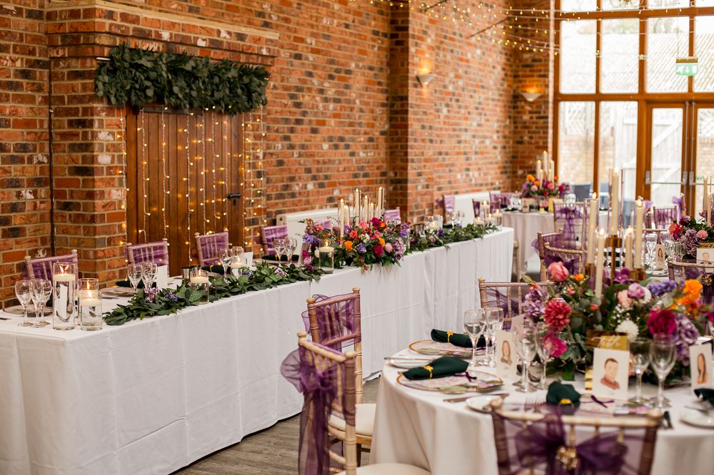 Elegant wedding reception tables with pink floral centerpieces and white linens in a rustic brick-walled venue.