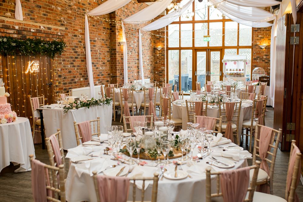 Elegant wedding reception venue with rustic brick walls and white-clothed round tables set for formal dining.