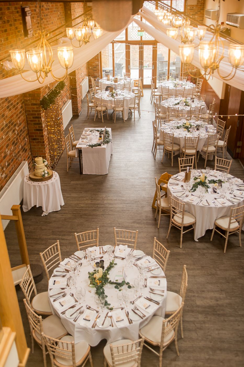 Elegant wedding reception venue with round tables, white linens, and crystal chandeliers in a rustic brick room.