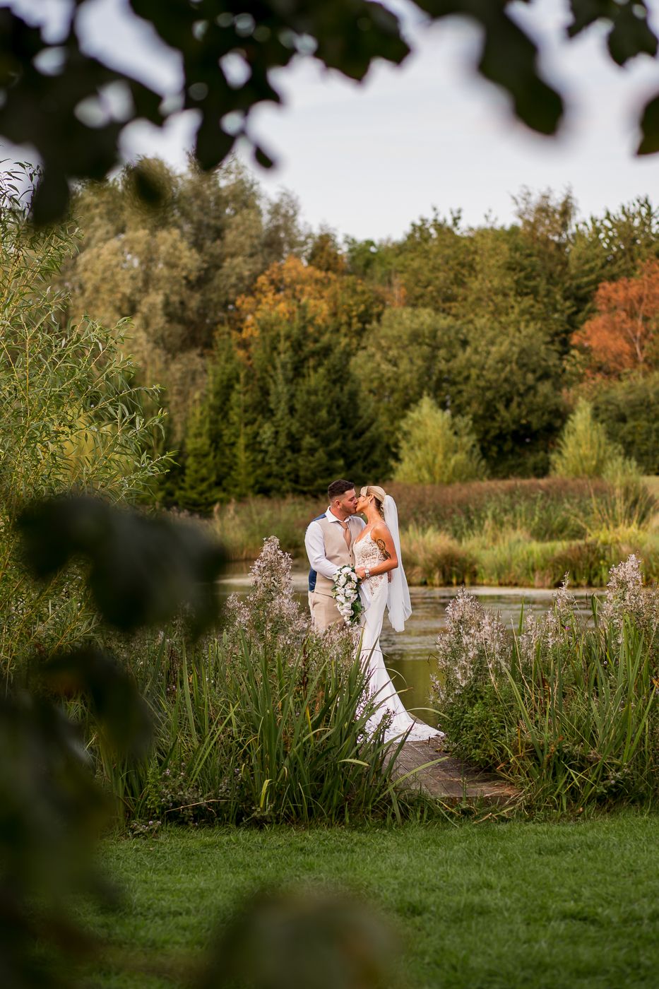 Romantic outdoor wedding photo of a couple embracing on a pathway surrounded by autumn foliage.