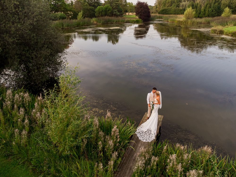 A scenic pond surrounded by lush greenery reflects trees and clouds in its calm waters on a summer day.
