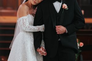 Wedding couple shares a tender moment while walking arm in arm in formal black tie and lace white dress attire.