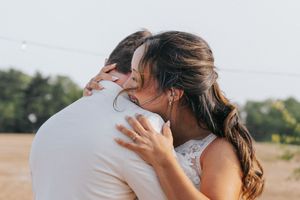 Couple embraces intimately while standing in an outdoor field with golden sunlight streaming through their hair.