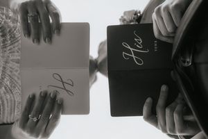 A hand holds a large perfume bottle while spritzing fragrance into the air in a black and white image.