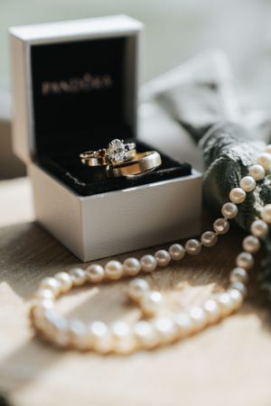 A string of elegant white pearls and wedding rings displayed with a black Pandora jewelry box.