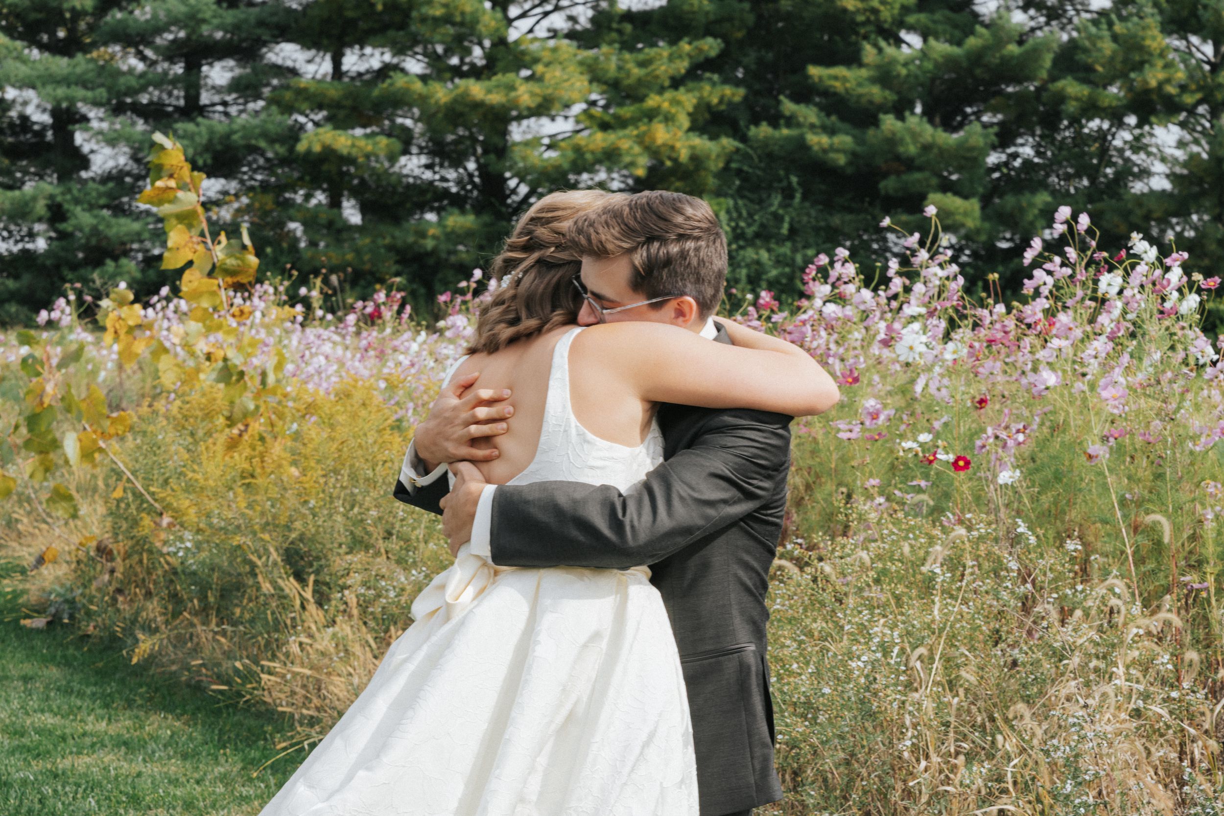 Couple embraces in a romantic garden setting surrounded by wildflowers and greenery on their wedding day.