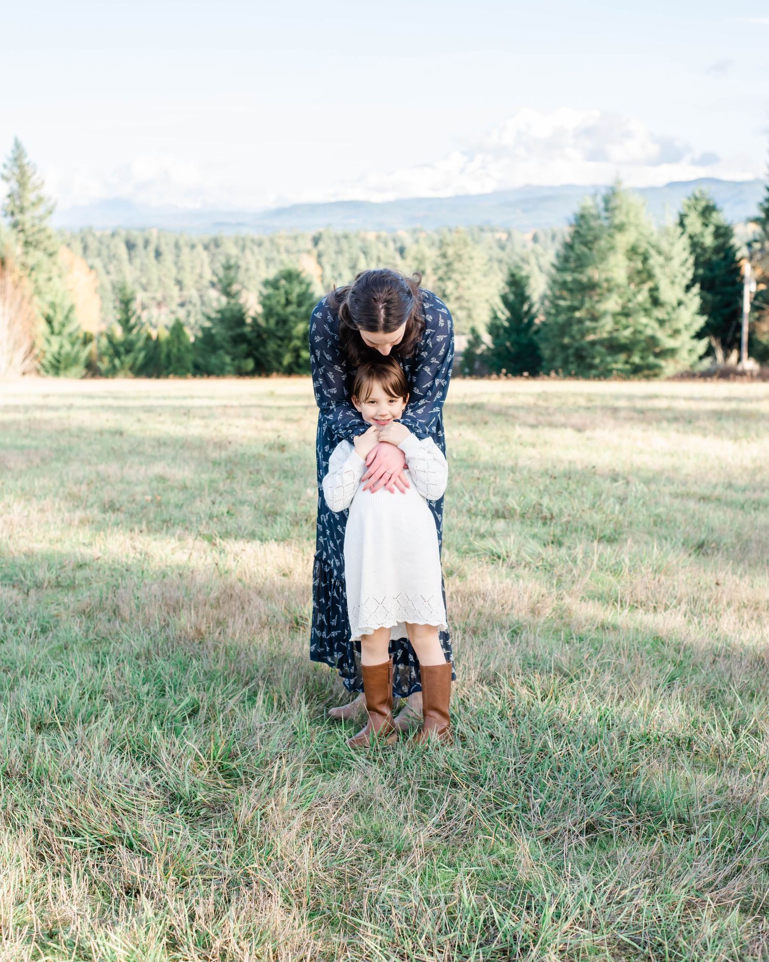 Intimate family portrait among tall grass with evergreen forest backdrop.