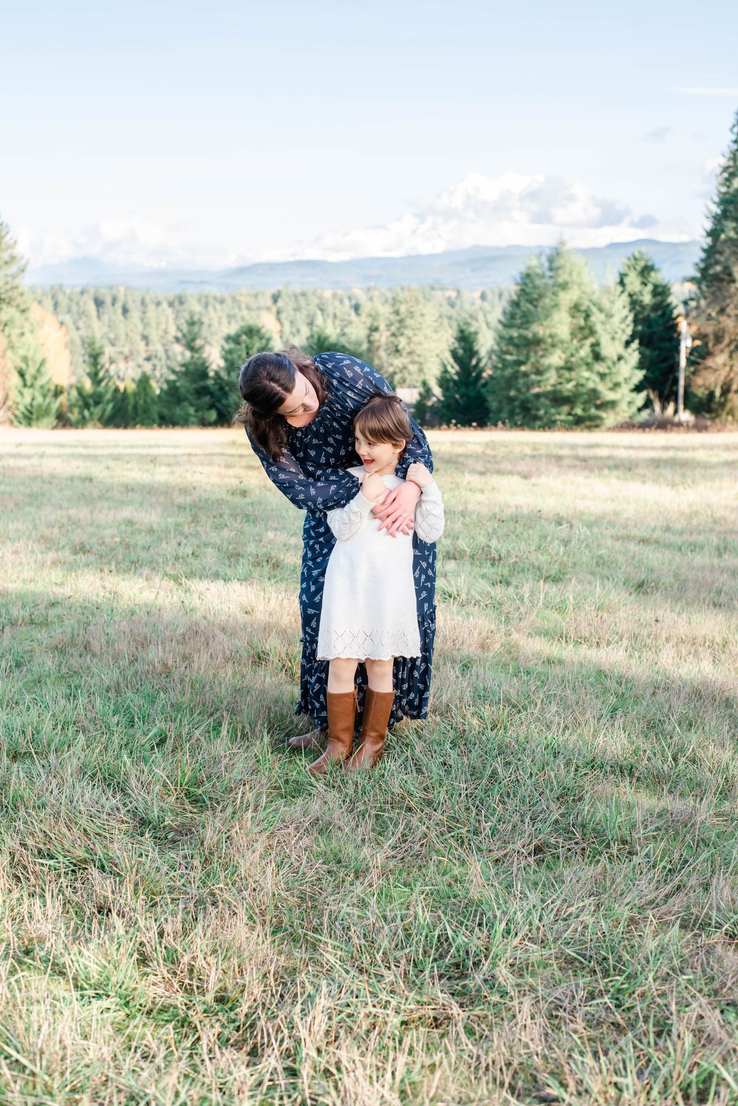 Two people embrace in a meadow wearing coordinating blue and white dresses with mountains in the distance.